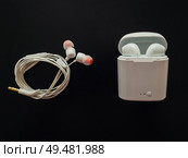 Comparison between classic wired headphones versus wireless earphones, air pods, isolated over black background. Pluses and minuses. Technology development tendencies, human conveniences concept. Стоковое фото, агентство Ingram Publishing / Фотобанк Лори