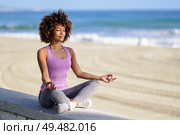 Black woman, afro hairstyle, doing yoga in the beach with eyes closed. Young Female wearing sport clothes in lotus figure with defocused background.. Black woman, afro hairstyle, in lotus asana with eyes closed in the beach. Стоковое фото, агентство Ingram Publishing / Фотобанк Лори