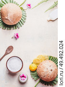 Coconut oil in wooden bowl with spoon and moisturizing cream on white desk background with tropical leaves and flowers , top view. Frame. Copy space. Flat lay. Modern skin care and cosmetic concept. Стоковое фото, агентство Ingram Publishing / Фотобанк Лори