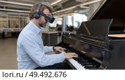 Man playing piano while wearing virtual reality headset in modern workspace. Мужчина играет на пианино, надев гарнитуру виртуальной реальности, в современном рабочем пространстве. Стоковое AI-изображение, AI-художник Katsiaryna Repich / Фотобанк Лори