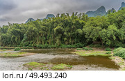 Puddles, shallow pools in the coastal area of the river. Thickets of green trees on the shore. Mountains in the distance against the sky and clouds. China. Li River. Li Jiang. Guilin. Стоковое фото, фотограф Вера Ивановна Кубарева / Фотобанк Лори