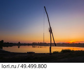 Idyllic rural scene with an old water well (popular called the stork well in the old villages of Moldova, also well sweep or shadoof). Calm sunset sky reflecting on the lake water surface. . Стоковое фото, агентство Ingram Publishing / Фотобанк Лори