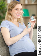 pregnant woman showing newborn shoes in living room. Стоковое фото, агентство Ingram Publishing / Фотобанк Лори
