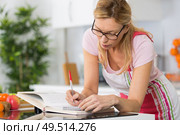mature woman reading cookbook in the kitchen looking for recipe. Стоковое фото, агентство Ingram Publishing / Фотобанк Лори