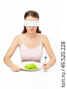 Girl blindfold sits before plate with salad leaf, isolated. Стоковое фото, агентство Ingram Publishing / Фотобанк Лори