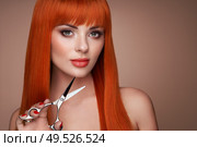 Beautiful young woman with a bright makeup and a smooth long hair holds metal scissors. Model with red hair. Hair salon, haircut. Care and beauty hair products. Perfect make-up. Стоковое фото, агентство Ingram Publishing / Фотобанк Лори