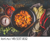 Homemade kimchi in black bowl on rustic background with ingredients: chinese cabbage , chili, spices and salt . Top view. Healthy fermented food. Стоковое фото, агентство Ingram Publishing / Фотобанк Лори