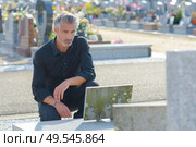 man placing flowers by headstone in cemetery. Стоковое фото, агентство Ingram Publishing / Фотобанк Лори