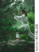 A woman dressed in a white kimono is standing confidently on a tree branch, showcasing a unique and daring pose. Стоковое AI-изображение, AI-художник Данила Большаков / Фотобанк Лори