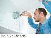 man fixing hanging cabinet door mechanism. Стоковое фото, агентство Ingram Publishing / Фотобанк Лори