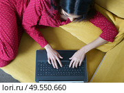 Young woman wearing pyjamas at home using laptop computer on a couch. Persian woman at home using laptop computer. Стоковое фото, агентство Ingram Publishing / Фотобанк Лори