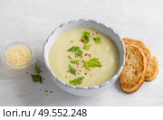Cream soup of stalked celery with cream, garnished with celery leaves, pink pepper and served with crispy toast on a light gray background, top view. Стоковое фото, фотограф Ольга Лепёшкина / Фотобанк Лори
