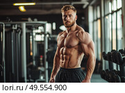 Shirtless muscular man standing in gym with intense gaze. Pumped up physique, six pack abs and strong pose in fitness club. Strength, bodybuilding and healthy lifestyle. Plenty of space for text. Стоковое AI-изображение, AI-художник Евгений Демидюк / Фотобанк Лори