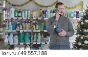 Handsome man speaking mobile and choose something in cosmetics store decorated for New Year holiday. Стоковое видео, видеограф Яков Филимонов / Фотобанк Лори