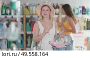 Joyful woman with a full basket of shopping, cleaning products and household chemicals in the supermarket. Customer looks at the shelves in the store against the background of other visitors. Стоковое видео, видеограф Яков Филимонов / Фотобанк Лори