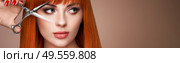 Beautiful young woman with a bright makeup and a smooth long hair holds metal scissors. Model with red hair. Hair salon, haircut. Care and beauty hair products. Perfect make-up. Стоковое фото, агентство Ingram Publishing / Фотобанк Лори