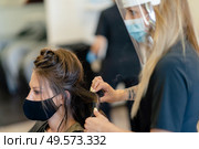 Hairdresser, protected by a mask, making waves in her client’s hair with a hair iron in a salon. Business and beauty concepts. Hairdresser, protected by a mask, combing her client’s hair with a hair iron in a salon. Стоковое фото, агентство Ingram Publishing / Фотобанк Лори