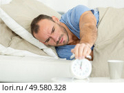 young man turning off the alarm clock on the bed. Стоковое фото, агентство Ingram Publishing / Фотобанк Лори