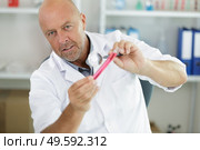 senior scientist looking at test tube through magnifying glass. Стоковое фото, агентство Ingram Publishing / Фотобанк Лори