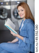 shot of a young woman reading a book in laundromat. Стоковое фото, агентство Ingram Publishing / Фотобанк Лори