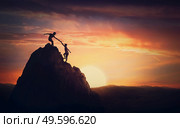 Scenery view with a team of two climbers on the top on the mountain. Person helping another to overcome obstacles and reach the top together. Teamwork concept, working in group to achieve success. Стоковое фото, агентство Ingram Publishing / Фотобанк Лори