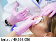 Aesthetic doctor injecting botox into the forehead of her middle-aged patient. Facial treatment done in a cosmetic surgery clinic.. Aesthetic doctor injecting botox into the forehead of her middle-aged patient. Стоковое фото, агентство Ingram Publishing / Фотобанк Лори