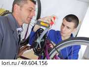 Young mechanic working on bicycle under supervision. Стоковое фото, агентство Ingram Publishing / Фотобанк Лори