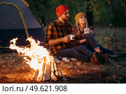 Young couple a guy and a girl in bright knitted hats stopped at a camping near the fire. Стоковое фото, агентство Ingram Publishing / Фотобанк Лори