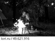 Young couple a guy and a girl in bright knitted hats stopped at a camping near the fire. Стоковое фото, агентство Ingram Publishing / Фотобанк Лори