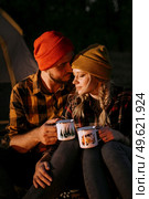 Young couple a guy and a girl in bright knitted hats stopped at a camping near the fire. Стоковое фото, агентство Ingram Publishing / Фотобанк Лори