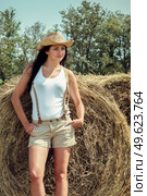 girl with black hair in beige wool coats and suspenders stands near the haystacks. Стоковое фото, агентство Ingram Publishing / Фотобанк Лори