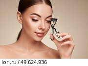 Close up of a beautiful young woman curling her eyelashes. Eyelash extensions. Стоковое фото, агентство Ingram Publishing / Фотобанк Лори