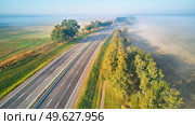 Sunny Magical autumn foggy morning. Aerial view of highway with cars. Asphalt road covered in fog. Early misty dawn. M1 magistaral in Belarus. Стоковое фото, агентство Ingram Publishing / Фотобанк Лори