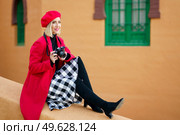 Middle-aged woman wearing red winter clothes, taking pictures with an SLR camera sitting on a city wall. Female wearing coat, skirt and beret outdoors.. Woman wearing red winter clothes, taking pictures with an SLR camera sitting on a city wall. Стоковое фото, агентство Ingram Publishing / Фотобанк Лори