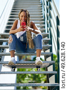 Young black woman, with coloured braids, watching something very funny on her smartphone. Girl with a skateboard.. Black woman, with coloured braids, watching something funny on her smartphone. Стоковое фото, агентство Ingram Publishing / Фотобанк Лори