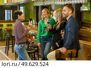 Gleeful diverse man and women with alcohol beverages smiling and talking while spending weekend day in bar together. Happy friends chatting in a beautiful bar. Стоковое фото, агентство Ingram Publishing / Фотобанк Лори