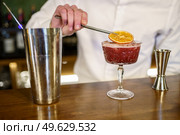 Unrecognizable male barkeeper putting dried slice of orange on top of cold fruit cocktail placed on counter in pub. Crop barman garnishing cocktail with citrus slice. Стоковое фото, агентство Ingram Publishing / Фотобанк Лори