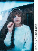 Sad woman alone in her home looking through a window in a rainy day. Стоковое фото, агентство Ingram Publishing / Фотобанк Лори