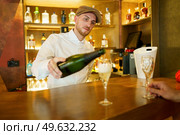 Elegant male bartender pouring sparkling champagne in glasses placed on wooden counter in luxury bar with crop unrecognizable client. Barman pouring drink in glasses in bar. Стоковое фото, агентство Ingram Publishing / Фотобанк Лори