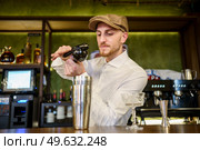 Bearded man in white shirt and cap squeezing lemon juice over shaker with cocktail while working behind counter in pub. Male barkeeper squeezing lemon into cocktail in a pub. Стоковое фото, агентство Ingram Publishing / Фотобанк Лори