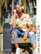 African woman with skateboard. Black girl relaxing after riding skateboard listening to the music outdoors.. African girl with skateboard relaxing after riding skateboard listening to the music. Стоковое фото, агентство Ingram Publishing / Фотобанк Лори