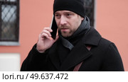 Handsome man wearing black coat and brown leather bag walking down on the city with mobile phone in hand. Stylish bearded middle-aged male using smartphone at urban street. Businessman going on job. Стоковое видео, видеограф Марина Демидюк / Фотобанк Лори