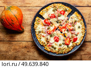 Pizza with salami, cheese, tomato on a pumpkin flatbread. Autumn recipe. Pumpkin-based pizza, wooden table. Стоковое фото, агентство Ingram Publishing / Фотобанк Лори