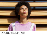 African-American woman getting sunlight on her face with her eyes closed, lost in thought, on a shutter of a modern building.. African-American woman getting sunlight on her face with her eyes closed. Стоковое фото, агентство Ingram Publishing / Фотобанк Лори