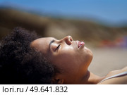 Side view of peaceful black female tourist with Afro dark hair, relaxing on sandy beach with closed eyes, and sunbathing on sunny day during summer holiday. Young African American woman lying on beach with closed eyes. Стоковое фото, агентство Ingram Publishing / Фотобанк Лори