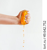 Woman hand squeezing halves of orange at white background with juice dripping. Front view. Стоковое фото, агентство Ingram Publishing / Фотобанк Лори