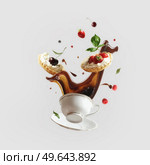 Creative levitation food concept with flying coffee splashing in cup and cakes with various berry and fruits at light background. Liquid in motion and sweet food in the air. Front view. Стоковое фото, агентство Ingram Publishing / Фотобанк Лори