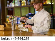 Bearded barman in white shirt and cap pouring liquor into shaker while preparing cocktail on counter in pub. Male barkeeper pouring alcohol into shaker. Стоковое фото, агентство Ingram Publishing / Фотобанк Лори