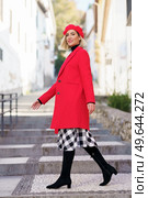 Full body of charming female in red beret looking at camera with smile while strolling on stone stairs in city. Stylish woman in coat walking on steps. Стоковое фото, агентство Ingram Publishing / Фотобанк Лори