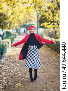 Full body of cheerful female in red coat and beret looking at camera while spinning around on walkway in autumn park. Happy woman spinning around on pathway. Стоковое фото, агентство Ingram Publishing / Фотобанк Лори